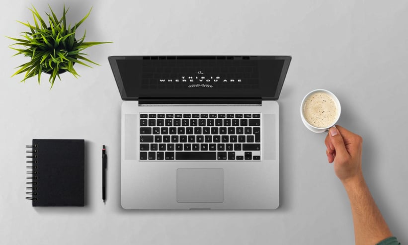 a hand holding a cup of coffee and a laptop on table